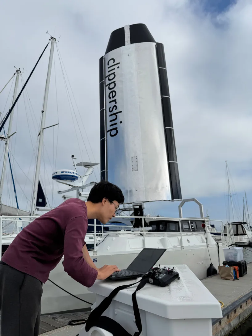 Operator at a laptop on deck, branded sail behind